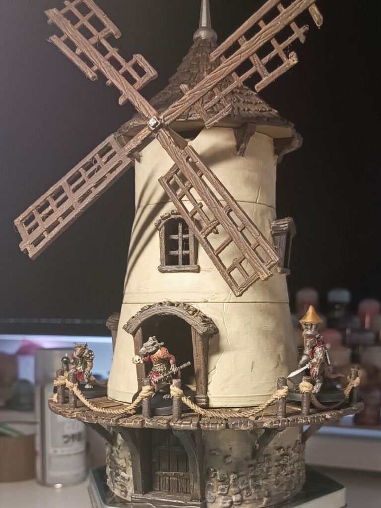 Wydrukowany model starego wiatraka otoczony figurkami szczurołaków.
